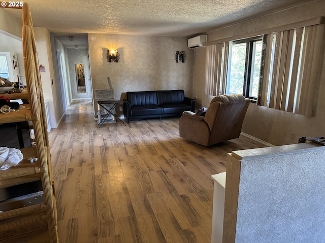 living room featuring wood finished floors, a textured ceiling, baseboards, and a wall mounted AC