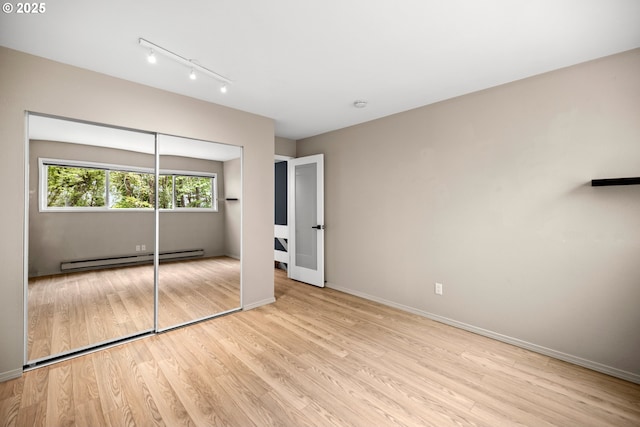 4360 SW Dickinson St Unit 35, Portland, OR 97219 - unfurnished bedroom featuring baseboard heating, light wood-style flooring, baseboards, track lighting, and a closet