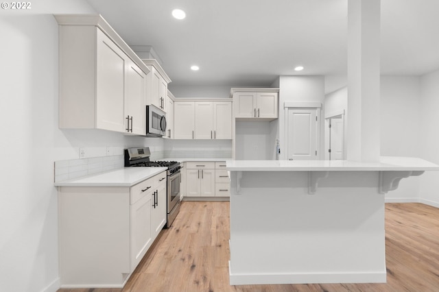 kitchen featuring light hardwood / wood-style flooring, appliances with stainless steel finishes, backsplash, white cabinets, and a kitchen bar