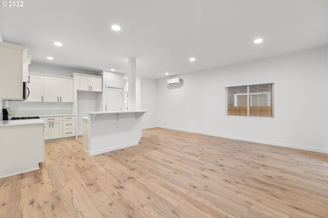 kitchen featuring a wall mounted air conditioner, light wood-type flooring, a kitchen breakfast bar, a kitchen island, and white cabinets