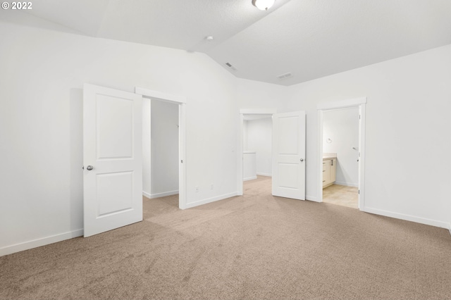 unfurnished bedroom with ensuite bathroom, lofted ceiling, and light colored carpet