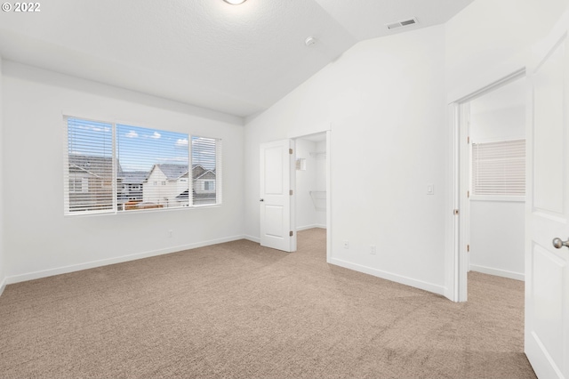 unfurnished bedroom with vaulted ceiling, a walk in closet, light colored carpet, a textured ceiling, and a closet