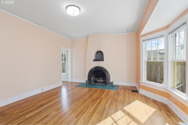 unfurnished living room featuring light wood-style flooring, ornamental molding, a healthy amount of sunlight, and a large fireplace