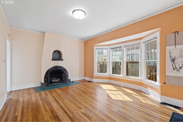 unfurnished living room with wood finished floors, baseboards, visible vents, a fireplace, and ornamental molding