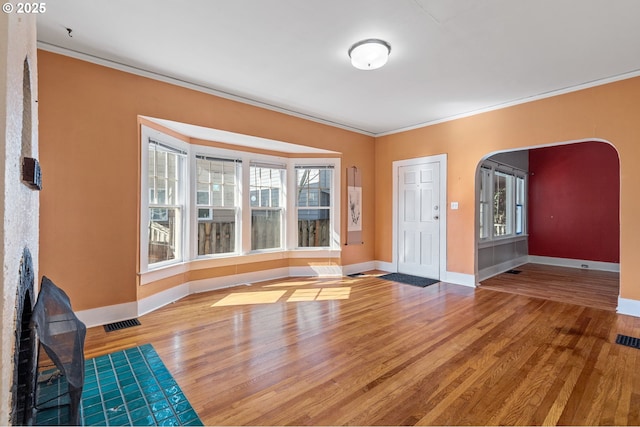 entryway featuring visible vents, ornamental molding, wood finished floors, arched walkways, and baseboards