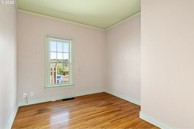 empty room with visible vents, ornamental molding, baseboards, and wood finished floors