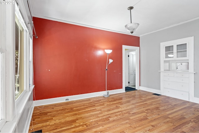 interior space with visible vents, wood finished floors, baseboards, and ornamental molding