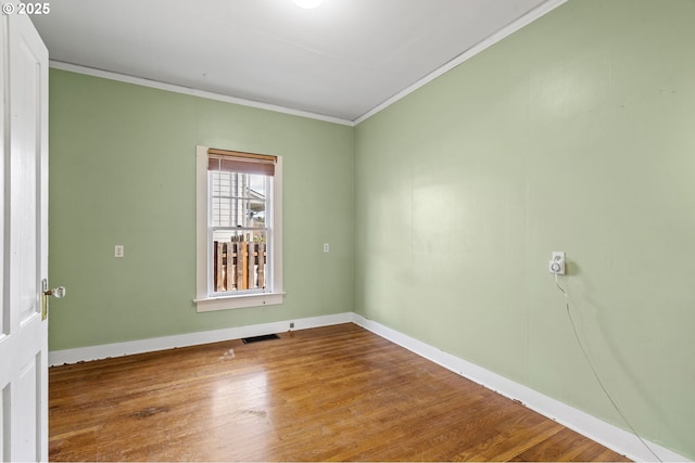 empty room with visible vents, baseboards, wood finished floors, and crown molding