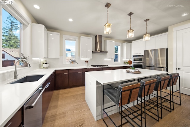 kitchen featuring sink, appliances with stainless steel finishes, dark brown cabinets, white cabinets, and wall chimney exhaust hood