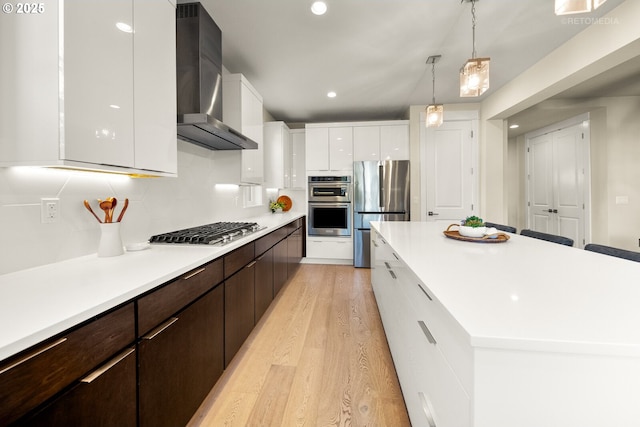 kitchen with stainless steel appliances, dark brown cabinetry, white cabinets, a kitchen island, and wall chimney exhaust hood