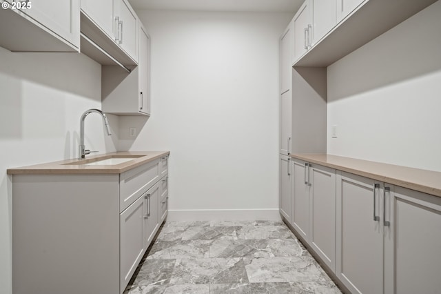 laundry room featuring a sink, light marble finish floors, and baseboards