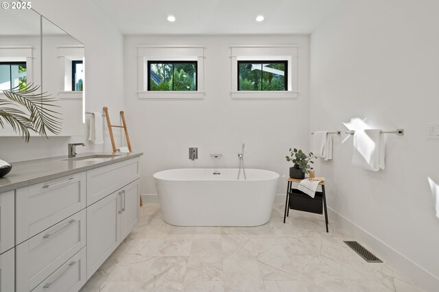 bathroom featuring a freestanding bath, healthy amount of natural light, baseboards, vanity, and recessed lighting