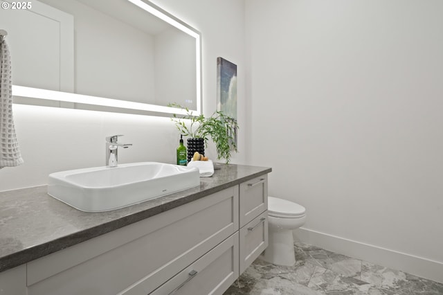 bathroom with marble finish flooring, vanity, toilet, and baseboards