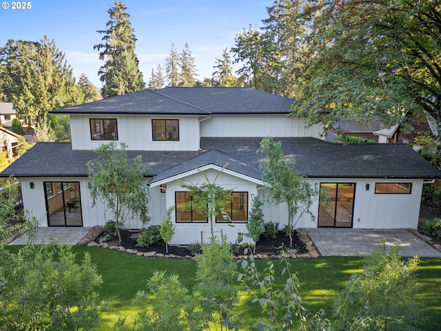 rear view of property with a patio, roof with shingles, and a yard