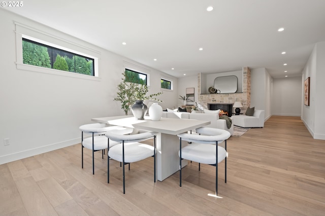 dining area featuring light wood-style flooring, recessed lighting, baseboards, and a stone fireplace
