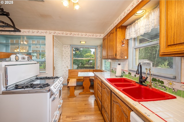 2822 Crocker Rd, Eugene, OR 97404 - kitchen featuring tile countertops, light wood-style flooring, wallpapered walls, brown cabinets, and gas range gas stove