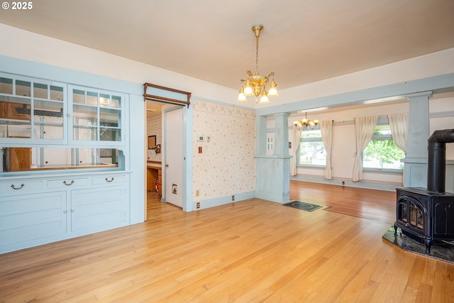2822 Crocker Rd, Eugene, OR 97404 - unfurnished living room with a chandelier, a wood stove, wood finished floors, wallpapered walls, and ornate columns