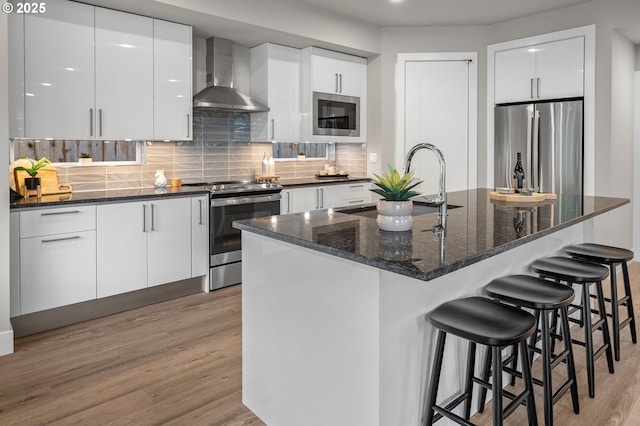 kitchen with stainless steel appliances, wall chimney exhaust hood, and modern cabinets