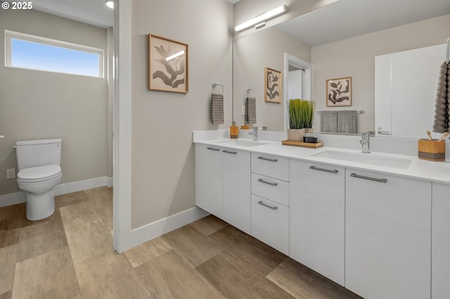 full bath featuring baseboards, a sink, toilet, and double vanity