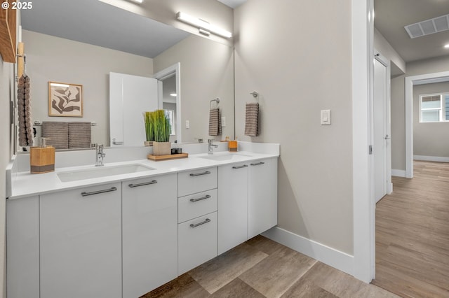 bathroom featuring double vanity, wood finished floors, a sink, and visible vents