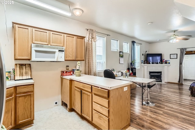 kitchen featuring white microwave, ceiling fan, open floor plan, a peninsula, and light wood-style floors