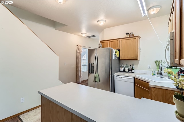 kitchen featuring visible vents, a sink, white appliances, a peninsula, and light countertops