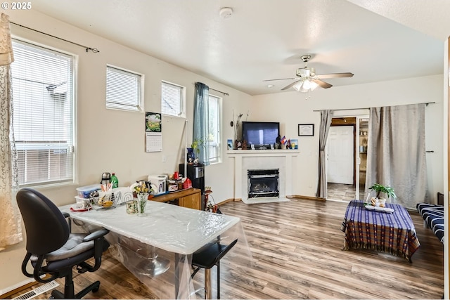 office with visible vents, a fireplace with flush hearth, wood finished floors, baseboards, and ceiling fan