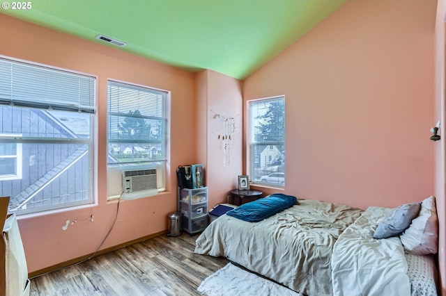 bedroom with visible vents, multiple windows, lofted ceiling, and wood finished floors