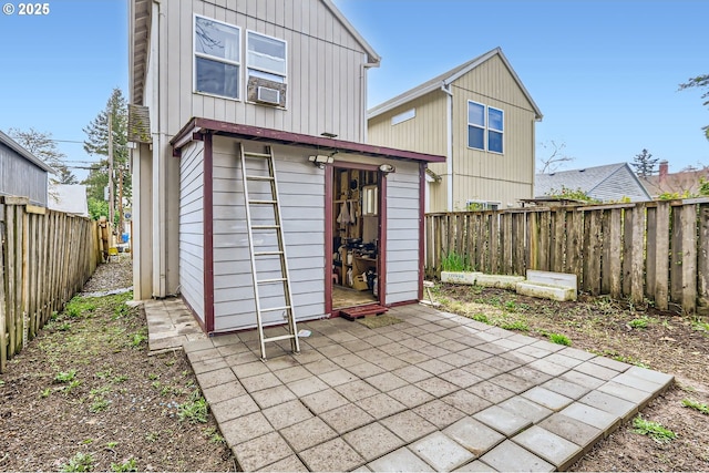 back of property with board and batten siding, cooling unit, an outdoor structure, a fenced backyard, and a patio area