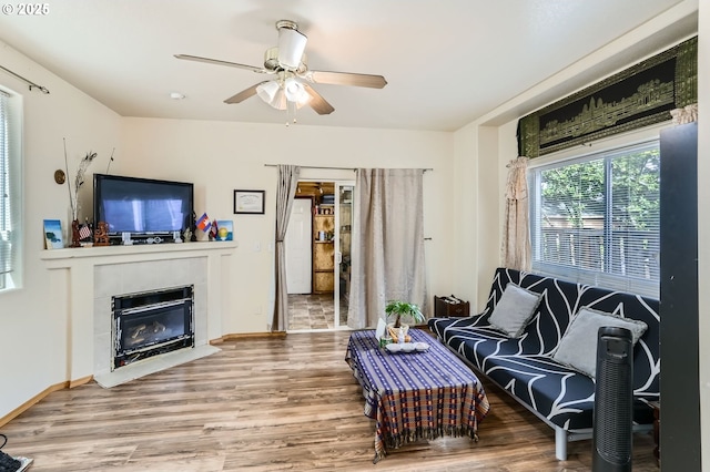 living room featuring baseboards, wood finished floors, a tile fireplace, and ceiling fan