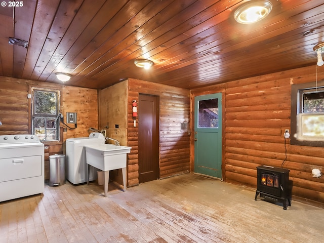 clothes washing area featuring light hardwood / wood-style floors, washing machine and clothes dryer, log walls, wooden ceiling, and a wood stove