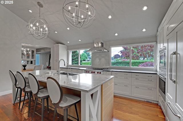 7100 SW Willowmere Dr, Portland, OR 97225 - kitchen with a chandelier, wall chimney exhaust hood, a sink, stainless steel appliances, and a kitchen island with sink