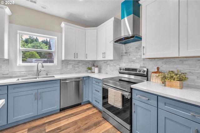 kitchen with wall chimney exhaust hood, sink, light hardwood / wood-style flooring, appliances with stainless steel finishes, and white cabinets