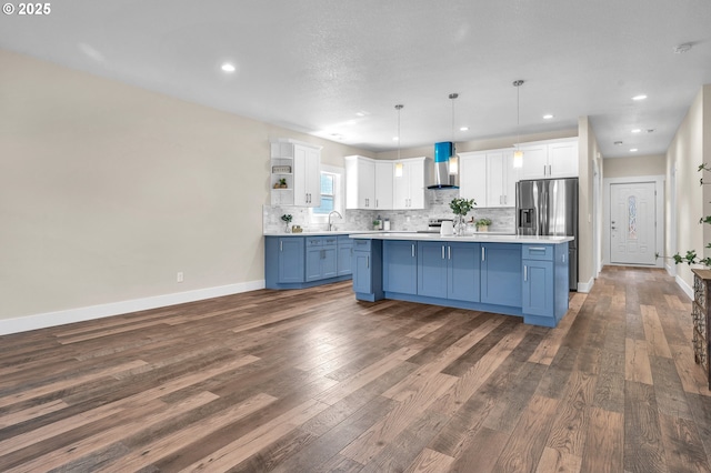 kitchen with pendant lighting, blue cabinets, stainless steel fridge, white cabinets, and wall chimney range hood