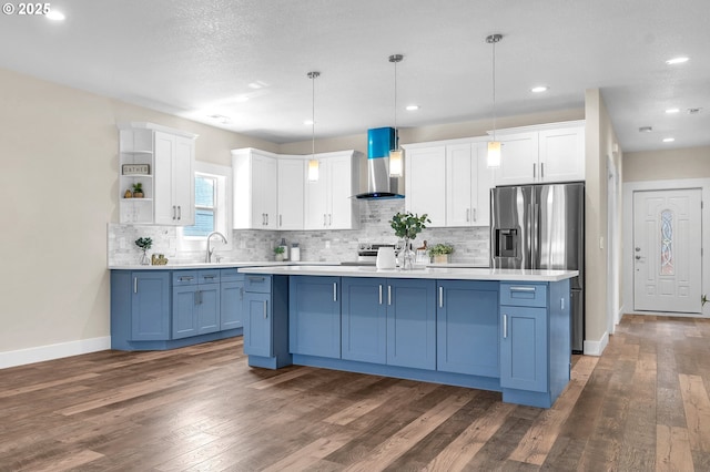 kitchen featuring pendant lighting, wall chimney range hood, blue cabinets, white cabinets, and a kitchen island