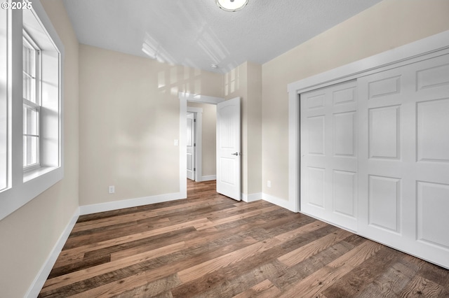 unfurnished bedroom with a textured ceiling, dark hardwood / wood-style flooring, and a closet