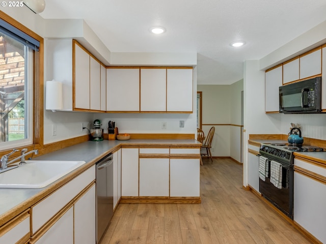 kitchen featuring light wood finished floors, light countertops, white cabinetry, a sink, and black appliances