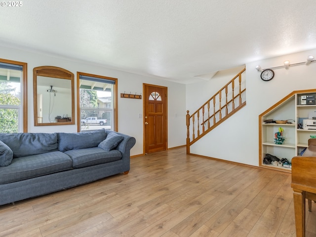 living area featuring a textured ceiling, stairway, light wood-type flooring, and baseboards