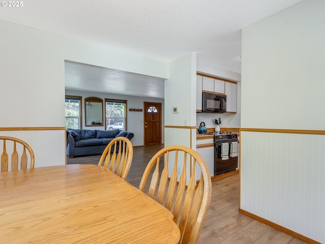 dining area featuring light wood-style floors, a wainscoted wall, and a textured ceiling