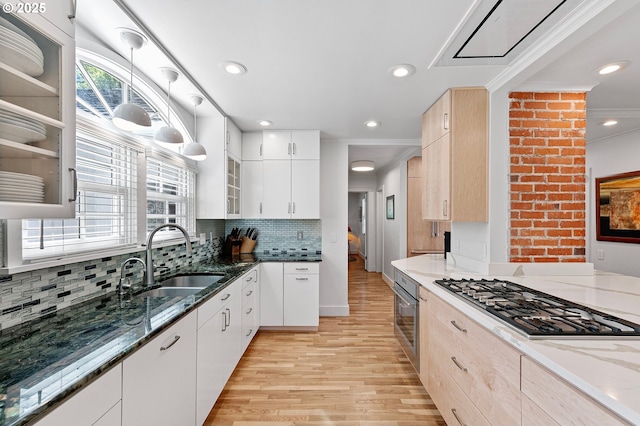 kitchen with appliances with stainless steel finishes, a sink, light wood-style flooring, stone counters, and glass insert cabinets