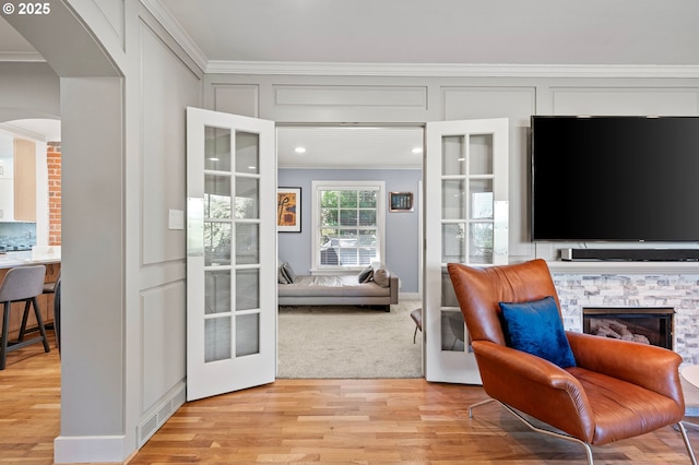 sitting room featuring crown molding, arched walkways, light wood finished floors, and a stone fireplace