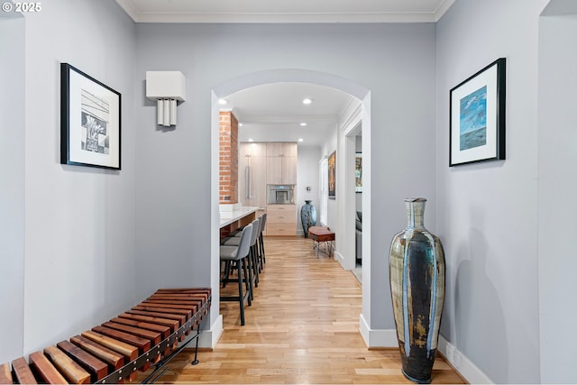 hallway with ornamental molding, arched walkways, light wood-type flooring, baseboards, and recessed lighting