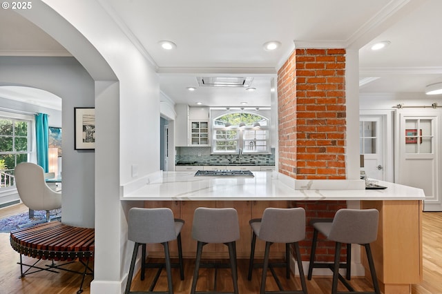 kitchen featuring light wood-type flooring, ornamental molding, stainless steel gas stovetop, decorative backsplash, and a sink