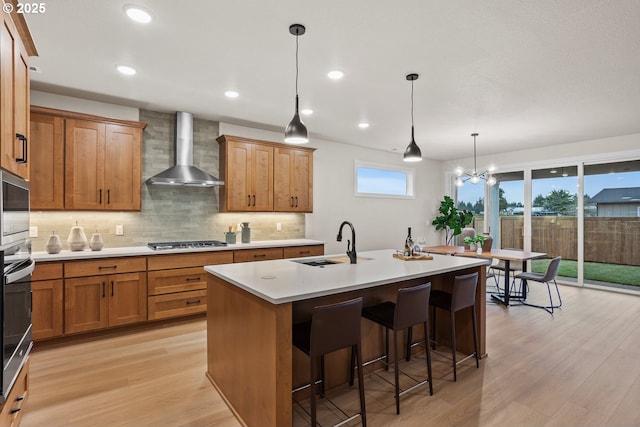 kitchen with a sink, light wood-style floors, wall chimney range hood, decorative backsplash, and stainless steel gas stovetop