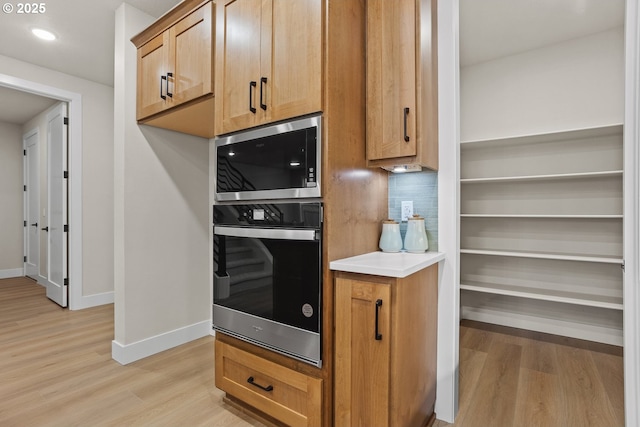 kitchen with baseboards, appliances with stainless steel finishes, light countertops, light wood-style floors, and backsplash