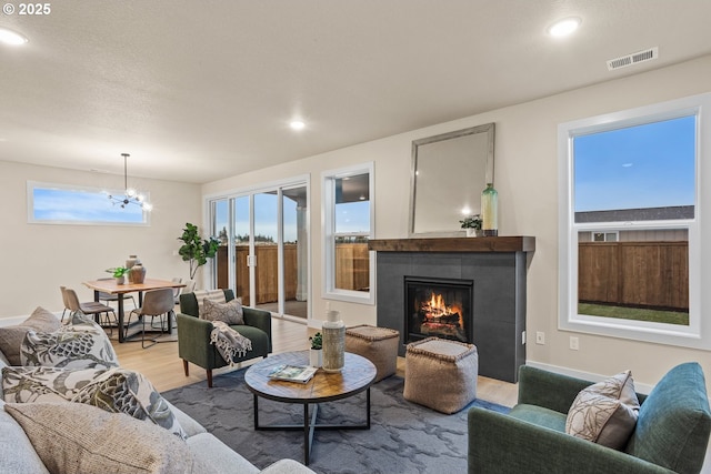 living room featuring baseboards, visible vents, a tiled fireplace, an inviting chandelier, and light wood-style floors