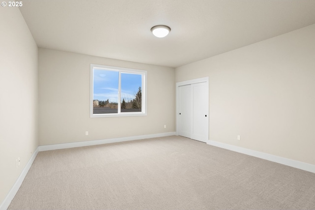 spare room featuring light carpet and baseboards