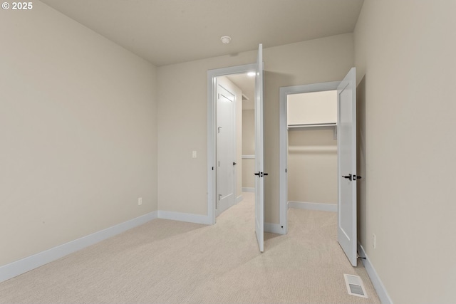 unfurnished bedroom with a closet, light colored carpet, visible vents, a spacious closet, and baseboards