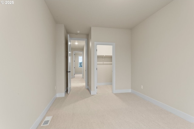 unfurnished bedroom with a closet, light colored carpet, visible vents, a spacious closet, and baseboards