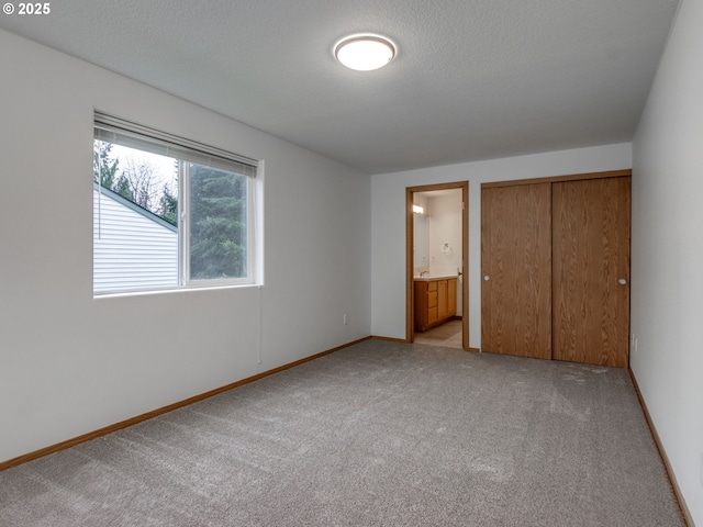 unfurnished bedroom with baseboards, ensuite bathroom, a closet, and light colored carpet